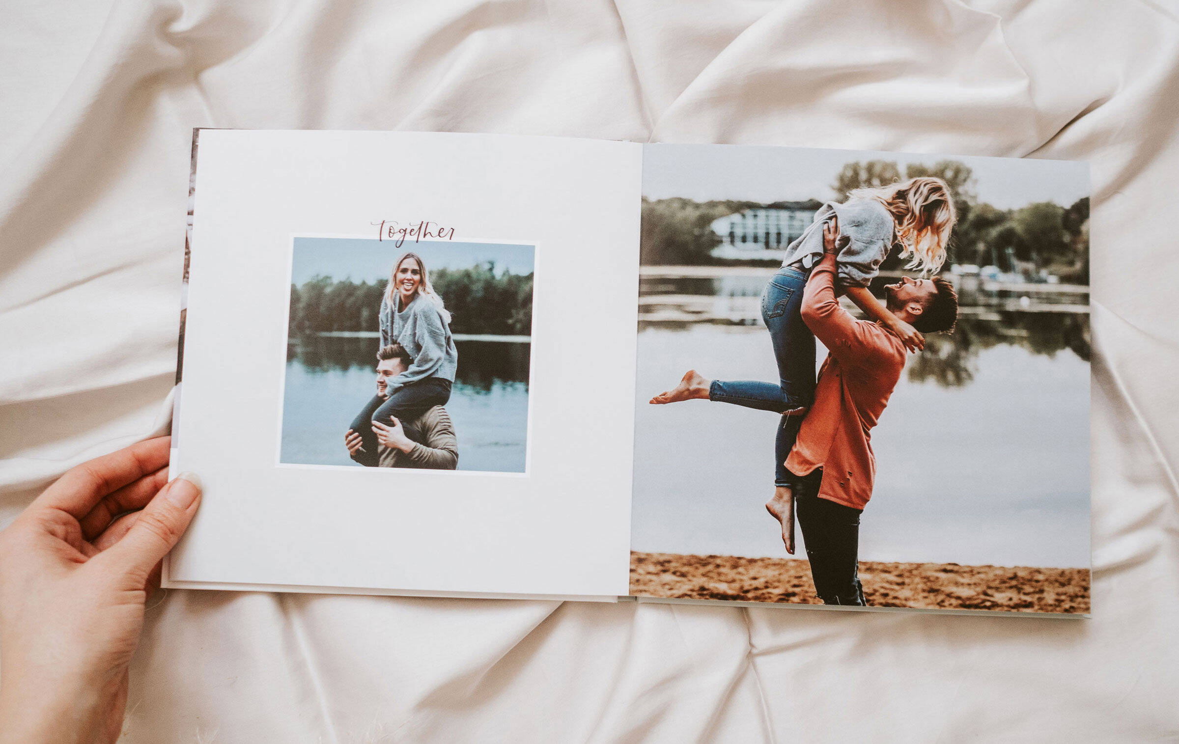 Ein CEWE FOTOBUCH liegt auf einer Decke und wird von einer Frauenhand aufgeschlagen. Zu sehen ist eine Doppelseite mit Fotos der Bloggerin Youdiful mit ihrem Freund und dem Clipart-Schriftzug "together".
